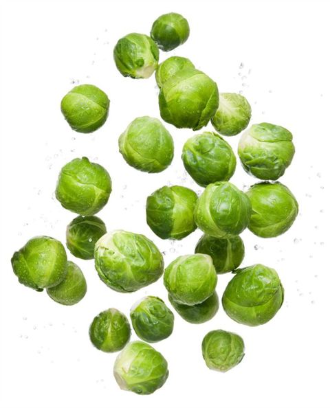 Sunn eating clean organic fresh vegetable brussel sprouts flying and bouncing up into the air in studio on a white background for wellness